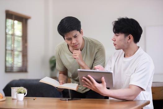 Young Gay Couple Sitting Together at Home, Engaging in a Discussion with a Book and Tablet photo