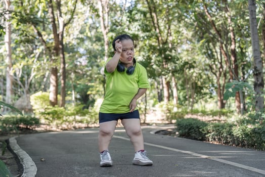 Exhausted Woman Jogging in Park Amidst Lush Greenery on a Sunny Day photo