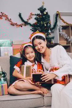 Merry Christmas and Happy Holidays. Cheerful mom and her cute daughter girl exchanging gifts. Parent and little child having fun near tree indoors. photo