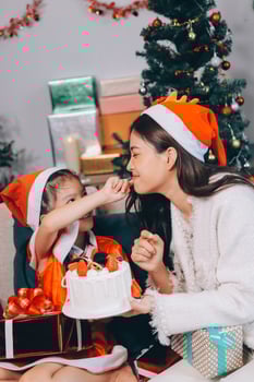 Merry Christmas and Happy Holidays. Cheerful mom and her cute daughter girl exchanging gifts. Parent and little child having fun near tree indoors. photo