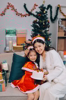 Merry Christmas and Happy Holidays. Cheerful mom and her cute daughter girl exchanging gifts. Parent and little child having fun near tree indoors. photo
