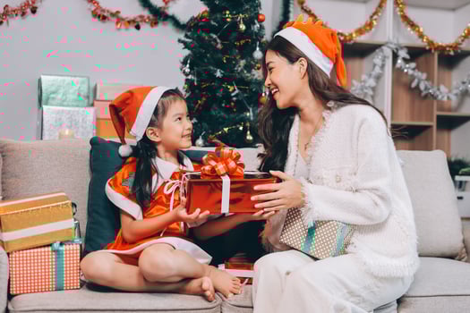 Merry Christmas and Happy Holidays. Cheerful mom and her cute daughter girl exchanging gifts. Parent and little child having fun near tree indoors. photo