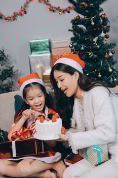 Merry Christmas and Happy Holidays. Cheerful mom and her cute daughter girl exchanging gifts. Parent and little child having fun near tree indoors. photo
