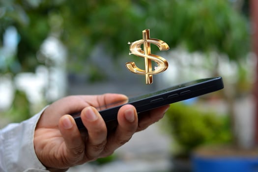 Gold colored dollar logo above a cellphone held by a man. photo