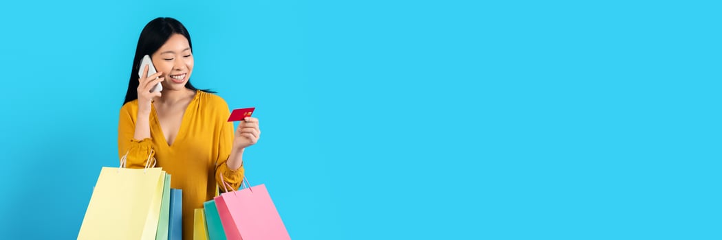 Shopping, phone call and credit card for ecommerce, information and confirmation. Happy young asian woman with shopping bags, talking on phone, holding bank card, calling bank to change limit photo