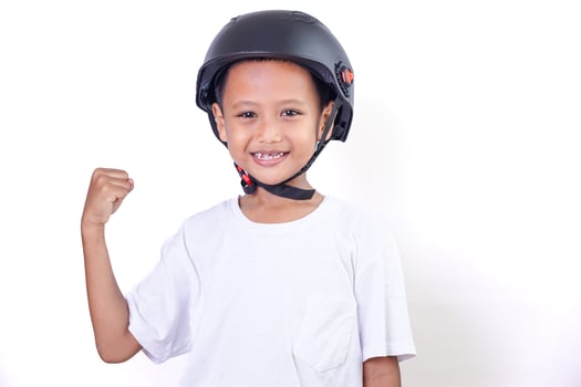 A cheerful asian child wearing a helmet, celebrating with raised fists and a bright smile. photo