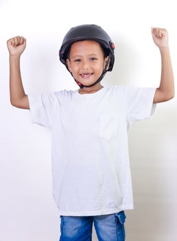 A cheerful asian child wearing a helmet, celebrating with raised fists and a bright smile. photo