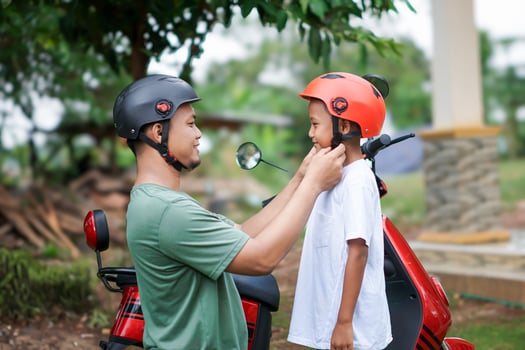 A asian father adjusts a child helmet for safety before riding a red electric scooter together outdoors. photo