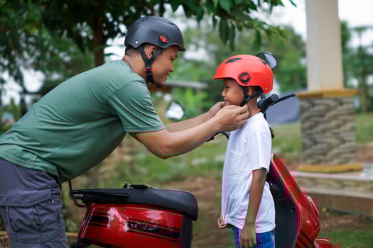 A asian father adjusts a child helmet for safety before riding a red electric scooter together outdoors. photo
