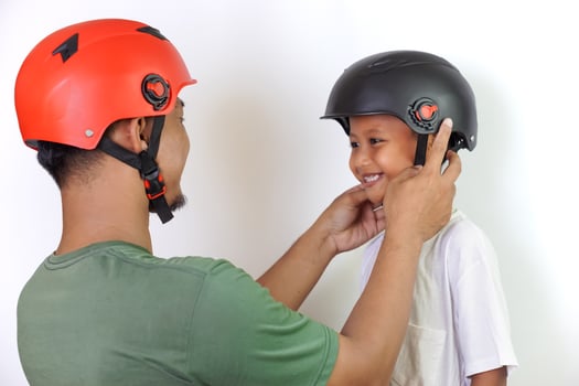 A asian father helps his son wear a helmet, ensuring safe and fun outdoor riding. photo