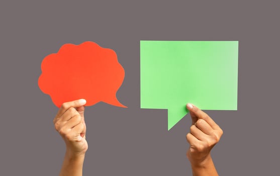 Close-up of hands holding a red and a green speech bubble against a gray background photo