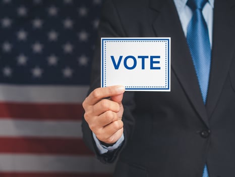 Close-up of hand voter holding paper with text VOTE while standing on the American flag background photo