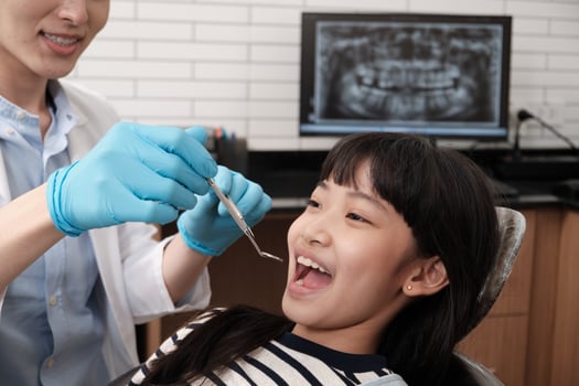 A young Asian male pediatric dentist checks and examines a little Thai girl's teeth in dental clinic, well-being mouth oral hygiene, and professional orthodontic healthcare work in a kid hospital. photo
