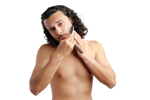 A man with curly hair grooming his beard in a well-lit space while using a straight razor photo