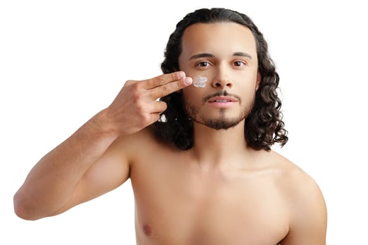 A young man demonstrates skincare routine with moisturizer on his face photo