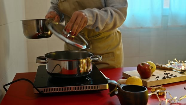 Person preparing mulled wine in a kitchen with fruits and spices photo