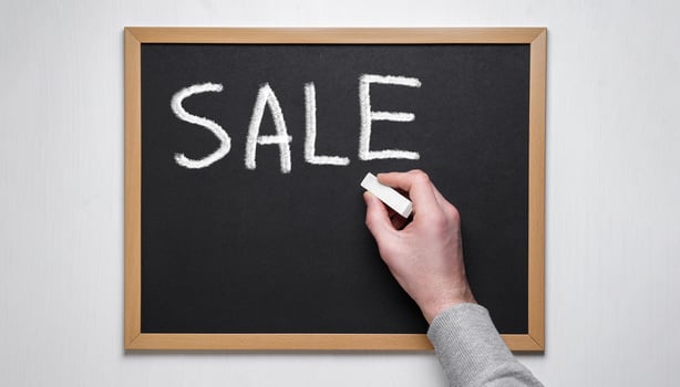 A hand holding a piece of chalk writes 'SALE' on a black chalkboard with a wooden frame, suggesting a promotional or discount event, ideal for marketing or retail stock photos. photo