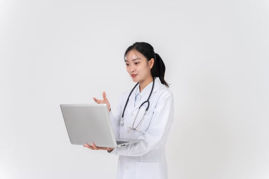 A female doctor stands against a studio background with her laptop, having an online consulting. photo
