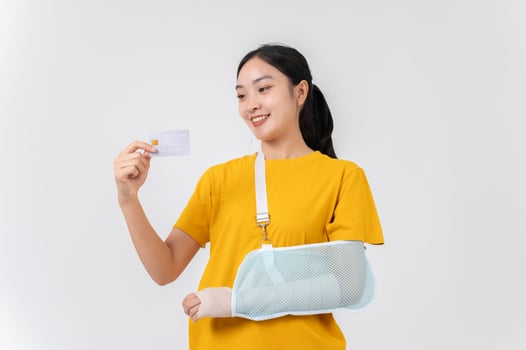 A carefree Asian woman with her broken arm, wrapped in a plaster bandage, holding her credit card. photo