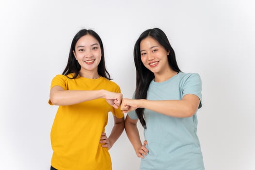Two young, beautiful Asian female friends doing a fist bump and smiling at the camera. photo