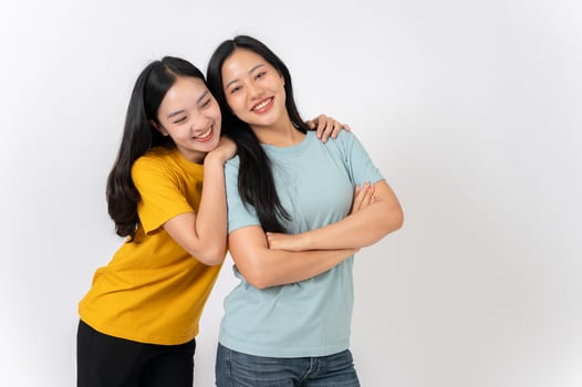 Two lovely, smiling young Asian women hugging while standing against on a white studio background. photo