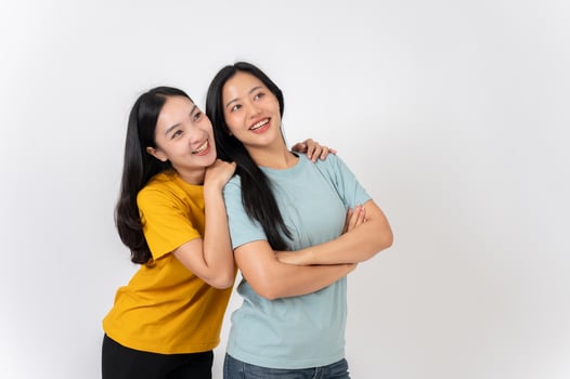 Two lovely, smiling young Asian women hugging while standing against on a white studio background. photo