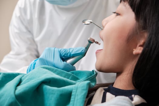 Asian female pediatric dentist checks and examines a little Thai girl's caries teeth in dental clinic, well-being mouth oral hygiene, and professional orthodontic healthcare work in a kid hospital. photo