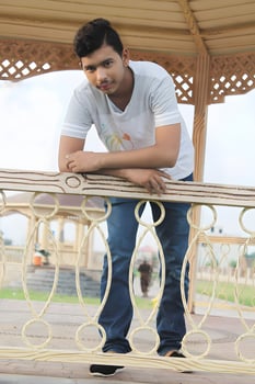Young Asian man leaning on the railing of a park bench, gazing directly at the camera with a friendly expression photo