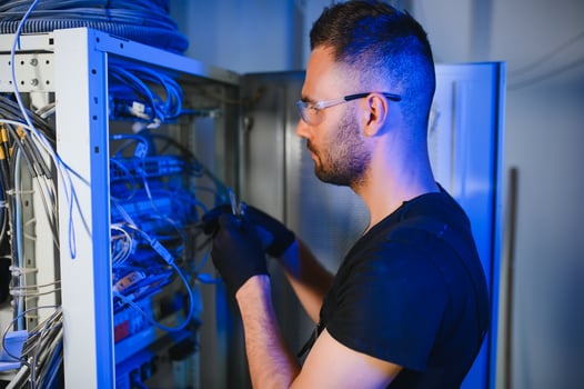 Young man is working with internet equipment and wires in server room photo