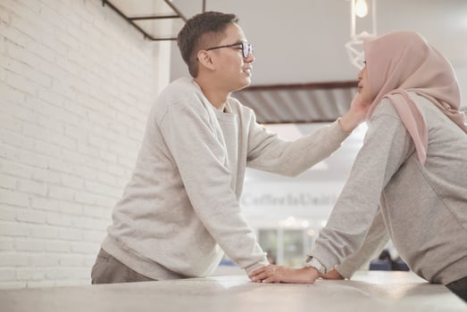 Married Asian Muslim couple looking at each other while sitting on the sofa together in the living room photo