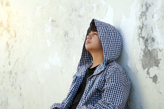 homeless young man with a hood over his head sits leaning against a wall. concept of homelessness, abandonment, sad, lonely, hopeless, depressed. photo
