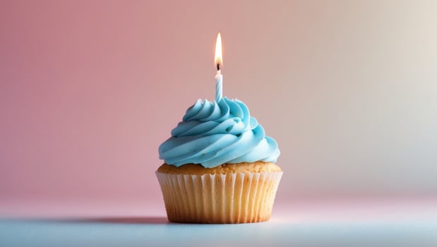 Bright cupcake with blue frosting and a single candle on a pink background for celebration photo