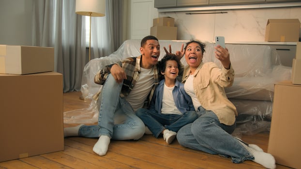 Happy joyful funny African American family parents mom dad little boy kid son child have fun together on floor at home weekend selfie photo on mobile phone camera smartphone blog celebrate moving day
