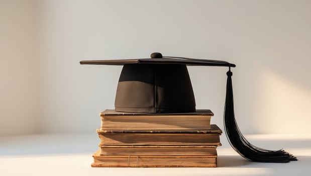 A graduation cap sits on top of a stack of books photo