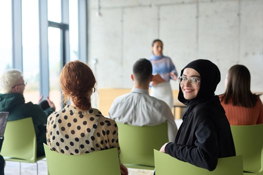 A diverse group of business professionals sits attentively in a modern office, actively participating in a training session led by an instructor, focusing on the latest technological advancements in photo