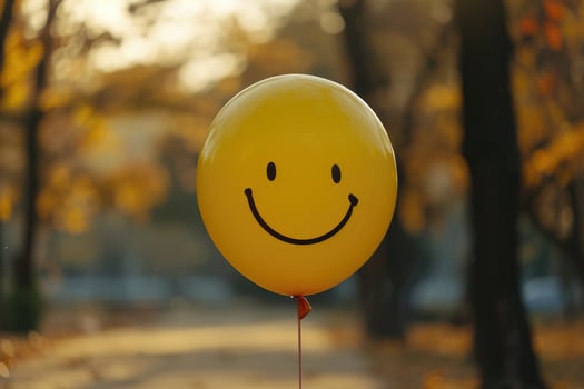 A yellow smiley face balloon is in the middle of a park photo
