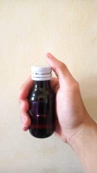 Hand holding a small dark bottle of medicine. photo