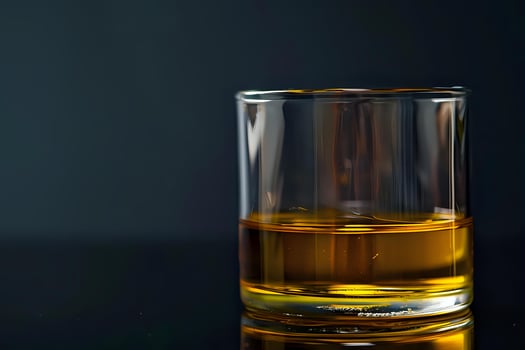 Golden Liquid in a Glass, Reflecting Light Beautifully, Displaying Clarity and Depth, on a Dark Surface, Evoking Sensations of Warmth and Smoothness. A Study in Still Life Photography with Amber Hues photo