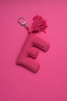 A pink crocheted keychain in the shape of the letter 'E' with a tassel, set against a matching pink background. photo