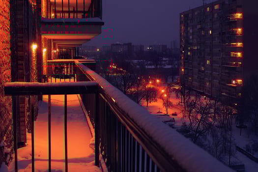 Cozy urban balcony view featuring snowfall and warm indoor lighting at twilight. photo