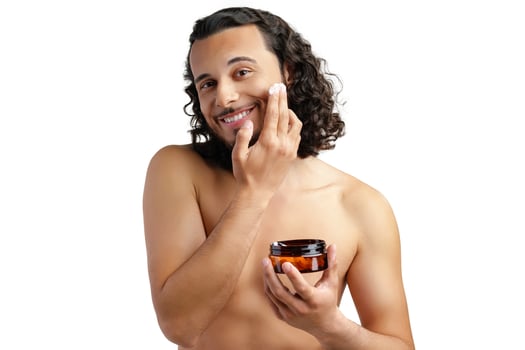 A young man applying skincare cream on his face with a focused expression, demonstrating personal grooming at home photo