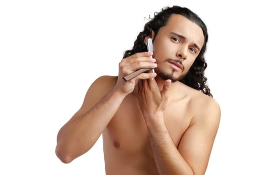 A man with curly hair grooming his beard in a well-lit space while using a straight razor photo