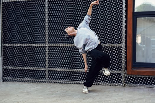 A dancer performs a move in front of a chain-link fence on a city street photo