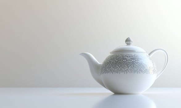 A white tea pot with a black and white design sits on a white table photo