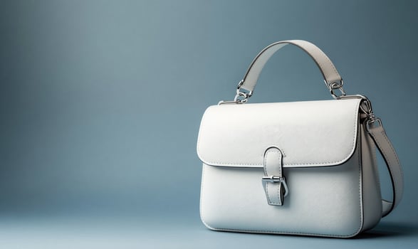A white purse with a gold clasp sits on a blue background photo