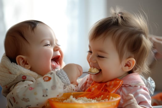 Two babies eating food from a bowl photo