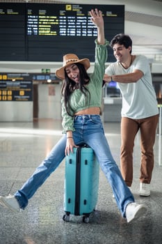 multicultural couple having fun at the airport sitting on top of suitcase photo