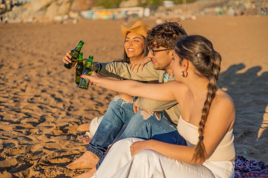 Multicultural Latin Friends Toasting with Beer Bottles on Beach at Summer Sunset photo