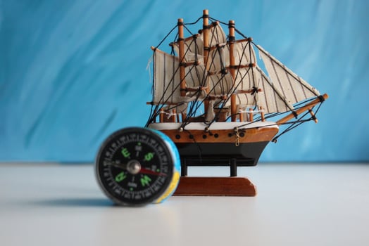 Wooden Sailing Ship Model And Vintage Compass On White Surface Over Blue Backdrop photo