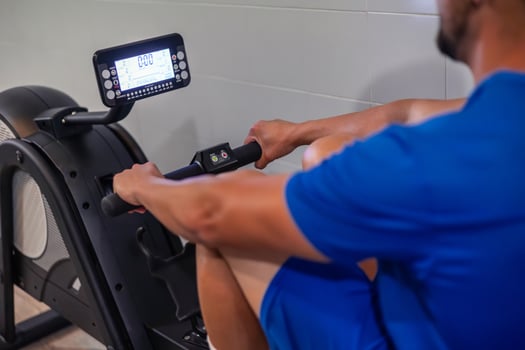 closeup of anonymous young athlete performing aerobic exercise on rowing machine in gym photo